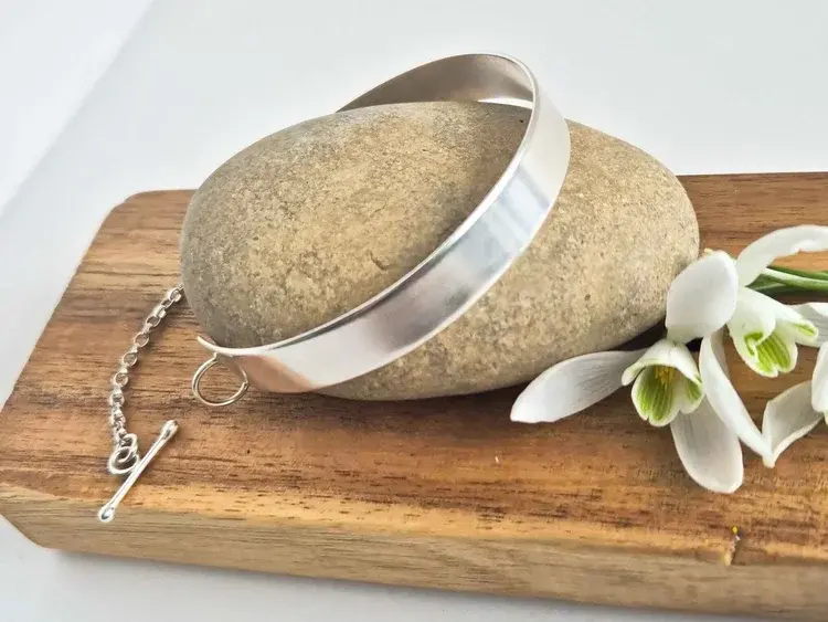 Silver bangle on pebble with snowdrops