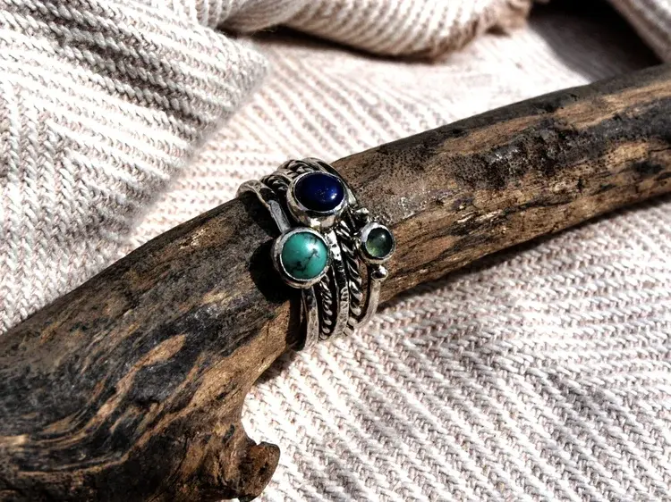 Stacked silver and gemstone rings on driftwood