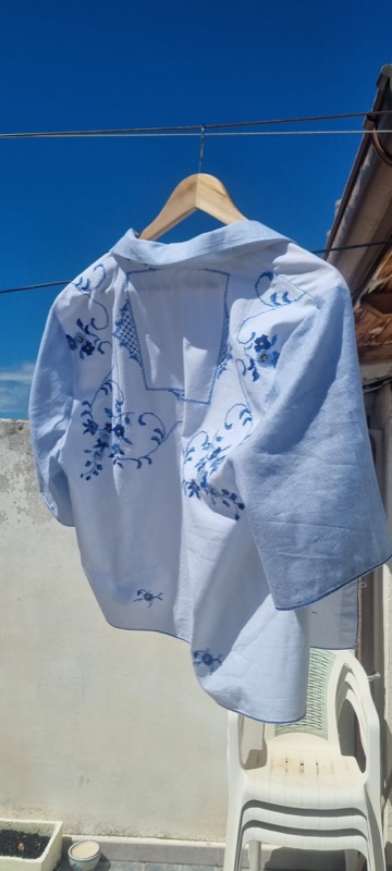 Blue cross-stitch embroidered linen blouse on a hanger