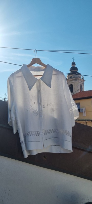 White linen blouse with cutwork detail, hanging against Mediterranean rooftops