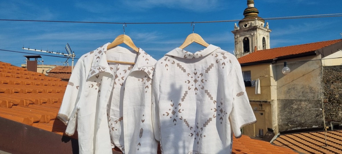 Two white embroidered linen blouses hanging against terracotta rooftops